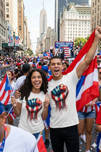 Two people celebrating with Puerto Rican flags and t-shirts in a city street.